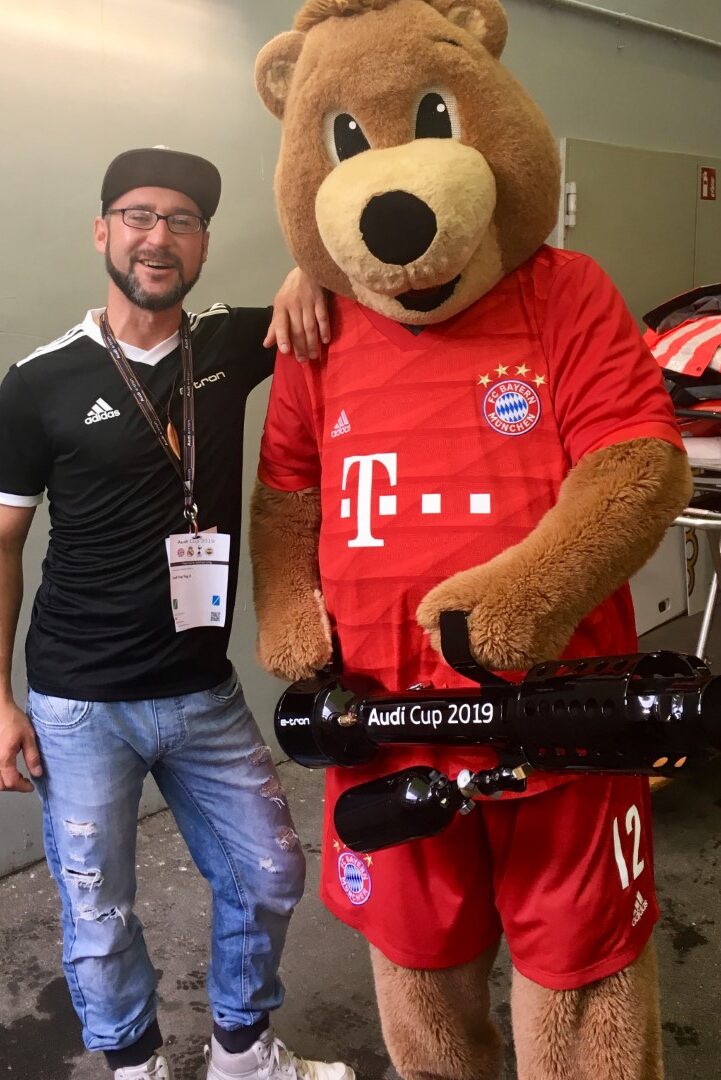 https://www.tshirt-kanonen.de/wp-content/uploads/2024/01/Fussball-FC-Bayern-Muenchen-Audi-Cup-2019-Maskottchen-T-Shirt-Kanone-Backstage-Bernie.JPG-Gross-e1705603926764.jpeg